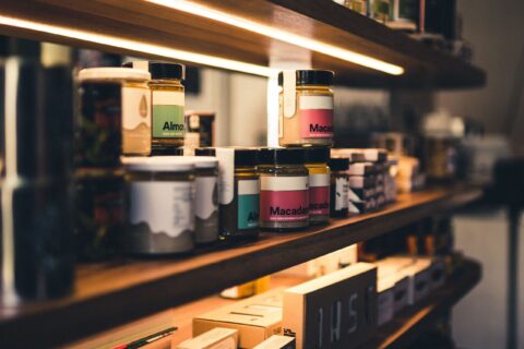 Close-up of artisan almond and macadamia nut butter jars on a wooden shelf in a shop.