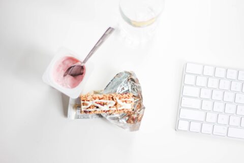 A stylish flat lay of yogurt and granola bar on a desk, perfect for a quick healthy snack.