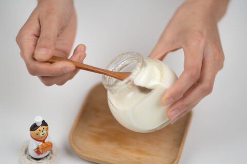 From above crop faceless male eating organic white yogurt from glass jar by using bamboo spoon