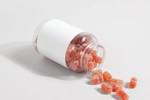 Close-up of gummy vitamins spilled from a clear bottle on a white surface